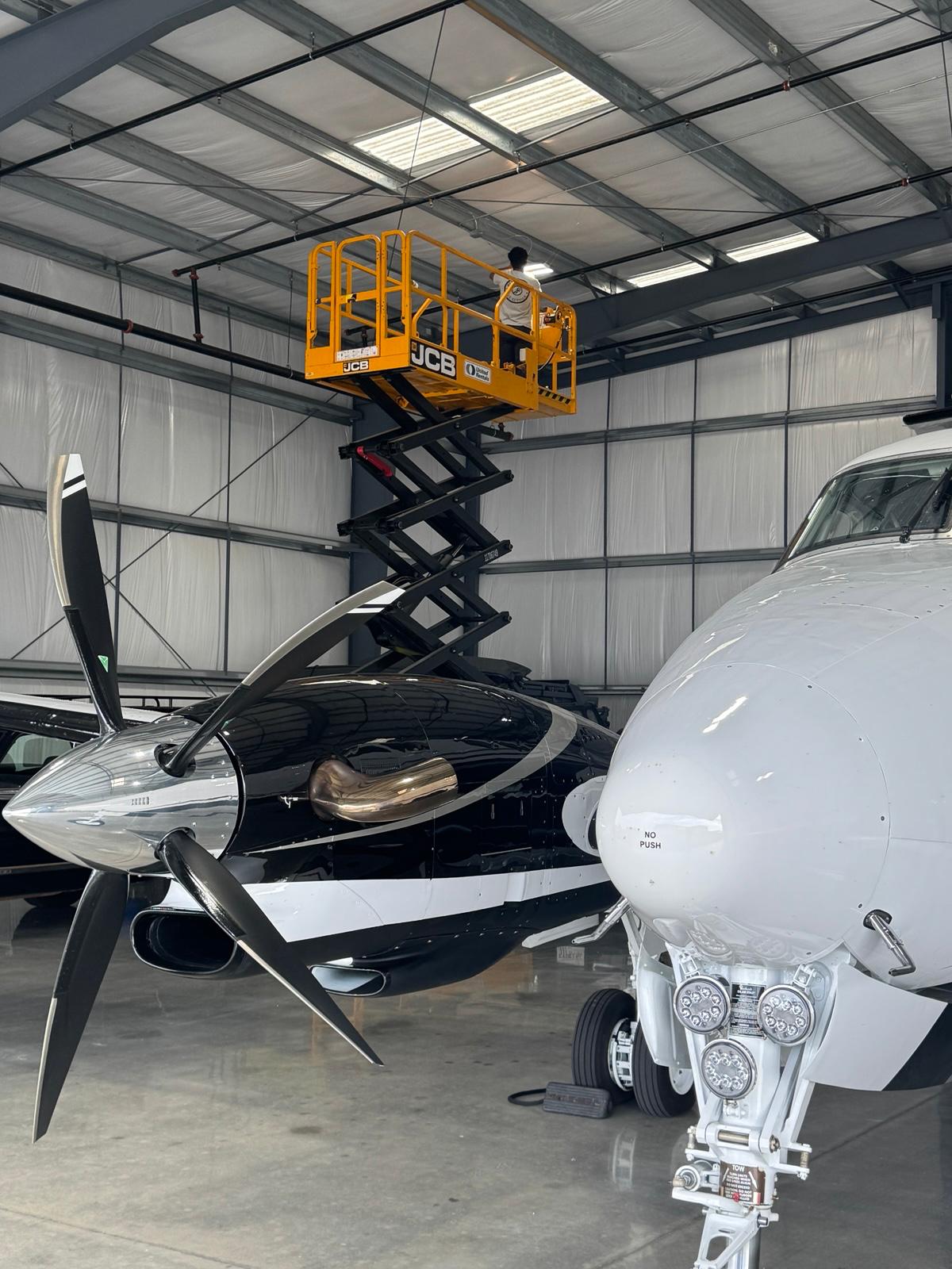 Professional LED ceiling installation in aircraft hangar with worker on scissor lift performing industrial lighting work